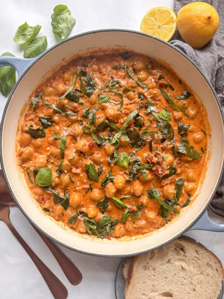 a casserole pan of marry me chickpeas, with sun-dried tomatoes, spinach, and basil in a creamy sauce