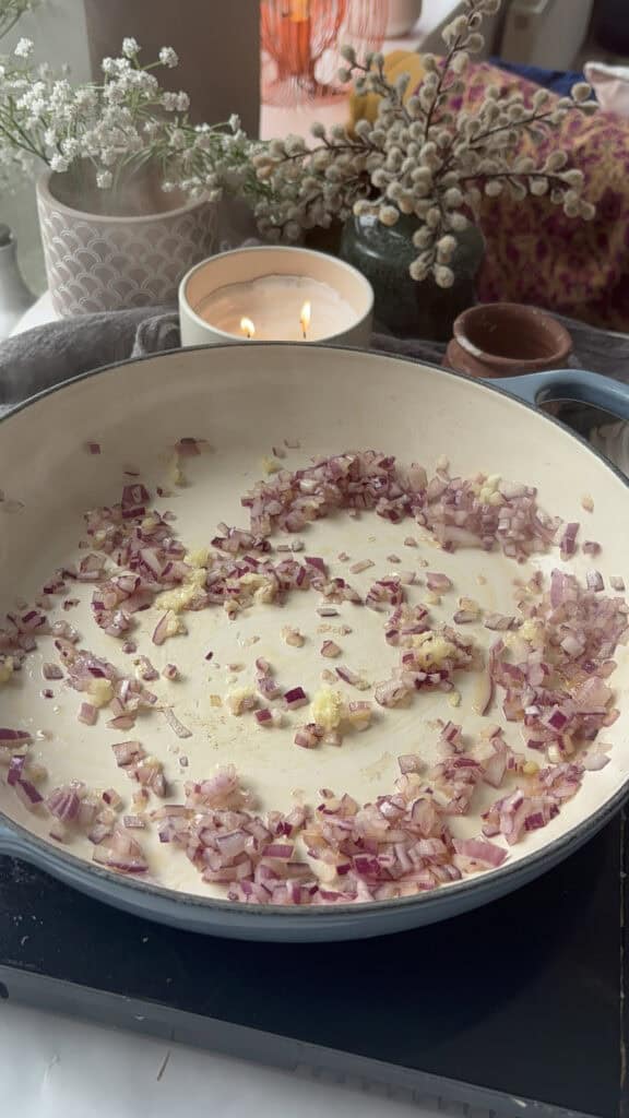 red onion and garlic being sauted in a casserole pan