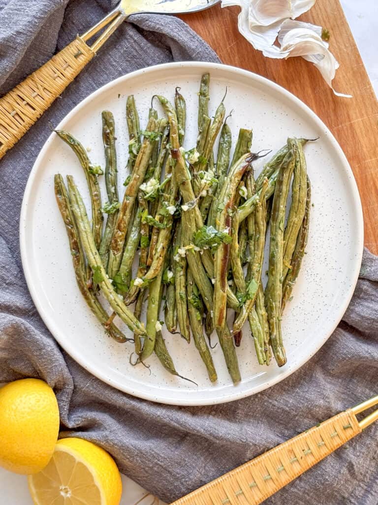 crispy roasted green beans on a small plate, topped with fresh parsley and garlic