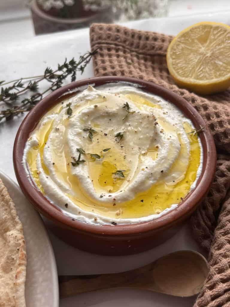 whipped ricotta in a bowl topped with olive oil, thyme, honey, lemon