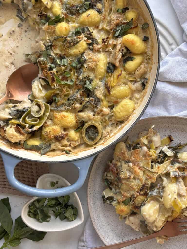 a casserole pan of the leek and gnocchi bake with a small plate with a portion on it to the side