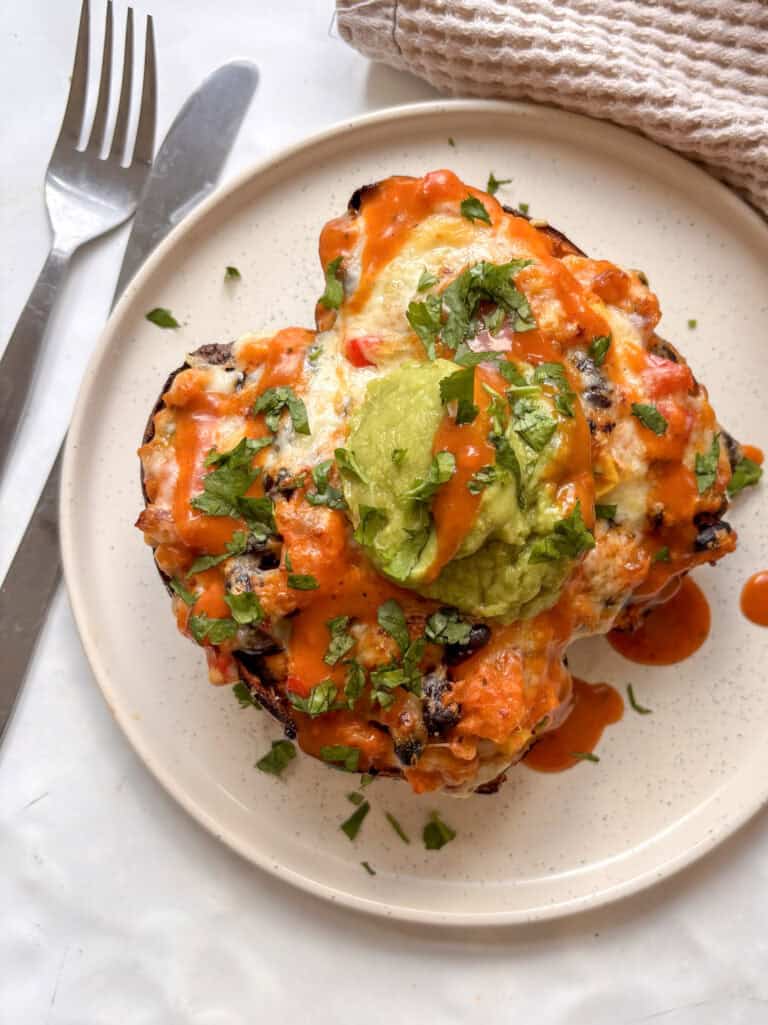 a white plate of mexican stuffed sweet potatoes topped with guacamole and cilantro