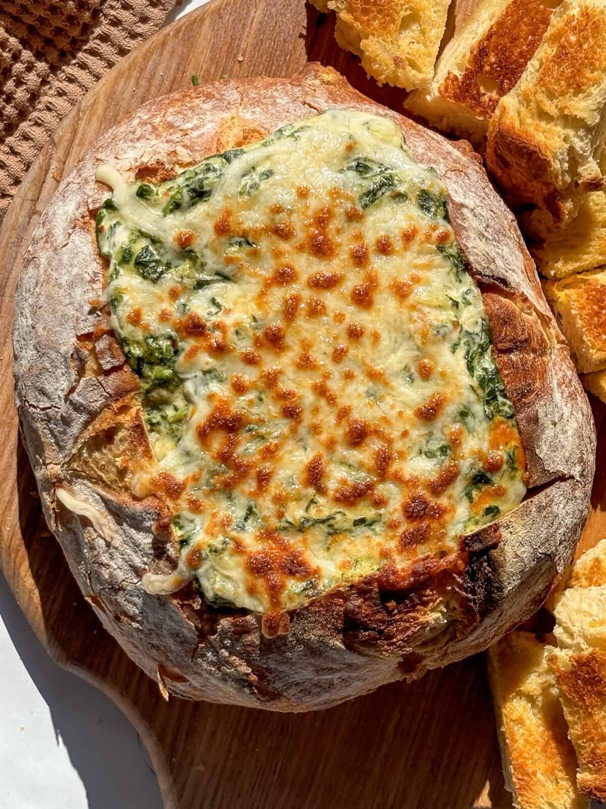 a hot spinach dip recipe with a cheesy melted topping, served inside a bread bowl