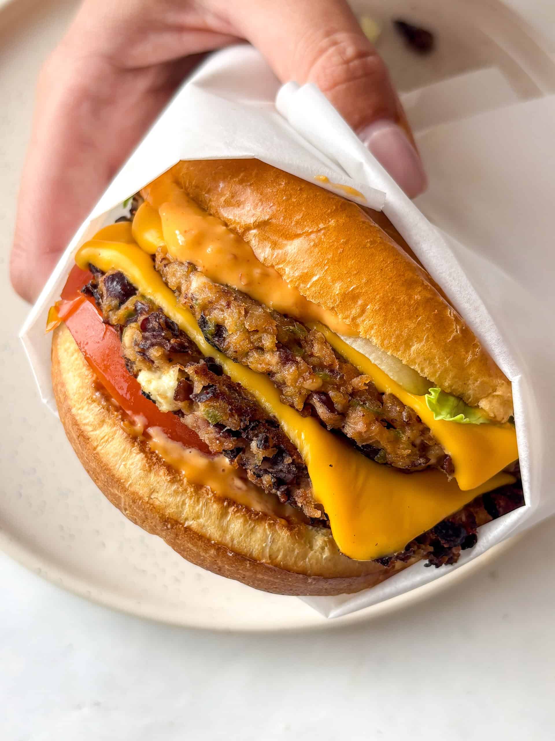 black bean burger - stacked with two black bean patties topped with melty American cheese, spicy mayo, sliced tomato, and lettuce in a toasted brioche bun