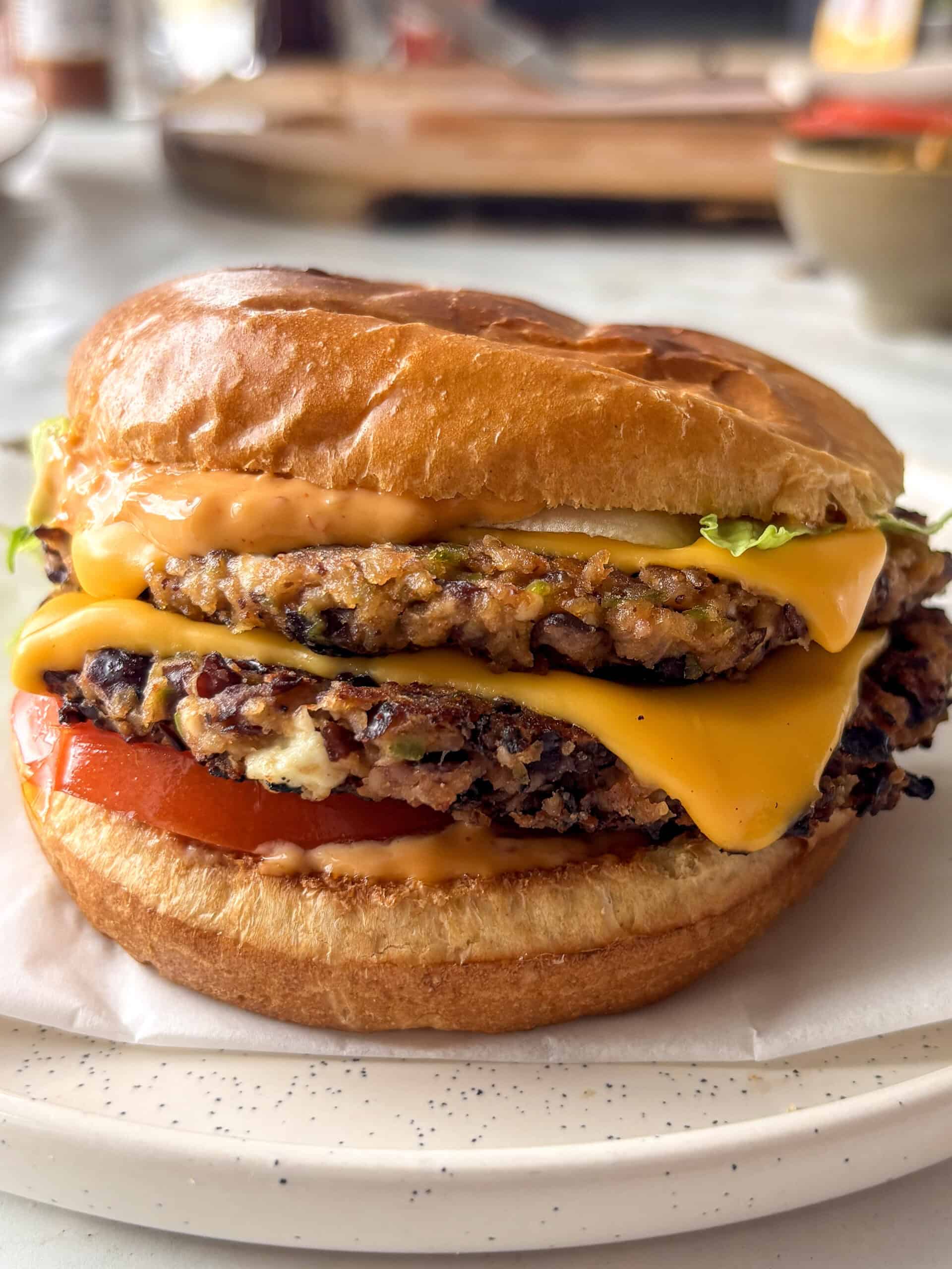 black bean burger - stacked with two black bean patties topped with melty American cheese, spicy mayo, sliced tomato, and lettuce in a toasted brioche bun