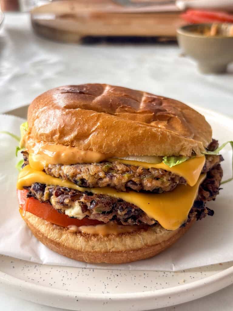 two black bean patties served in a toasted brioche bun with cheese, tomato, lettuce, and a spicy chipotle sauce
