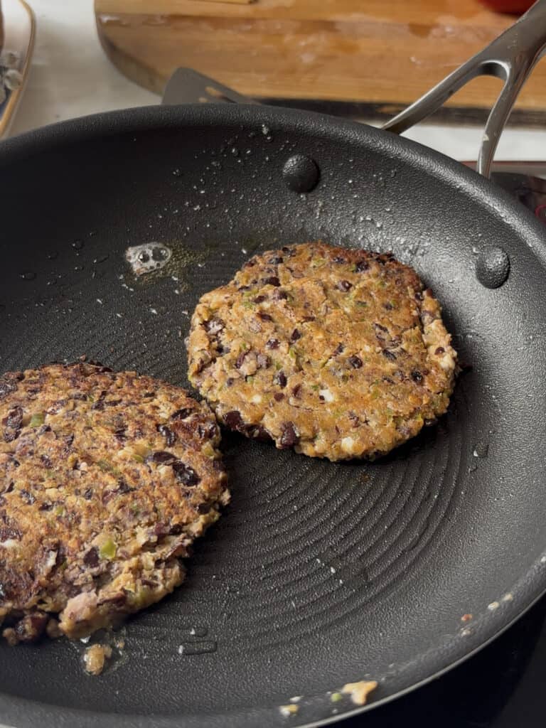 two black bean patties being fried in a little oil in a saucepan