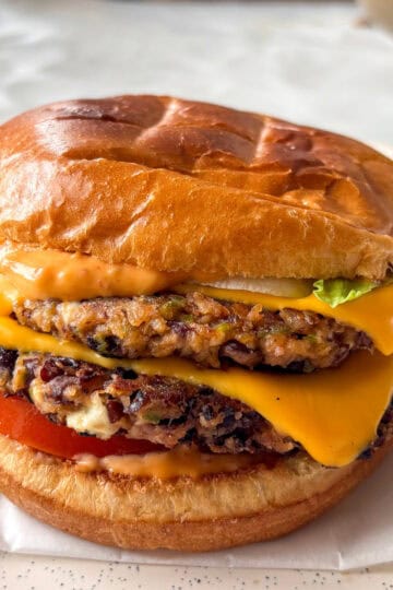 black bean burger - stacked with two black bean patties topped with melty American cheese, spicy mayo, sliced tomato, and lettuce in a toasted brioche bun