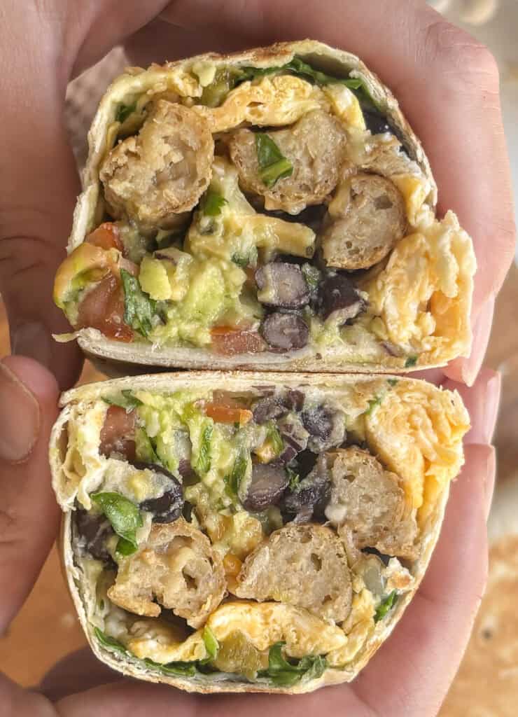 breakfast burritos stacked up on each other, cut in half to show the crossection of vegetartian sausages, egg, black beans, spinach, avocado etc