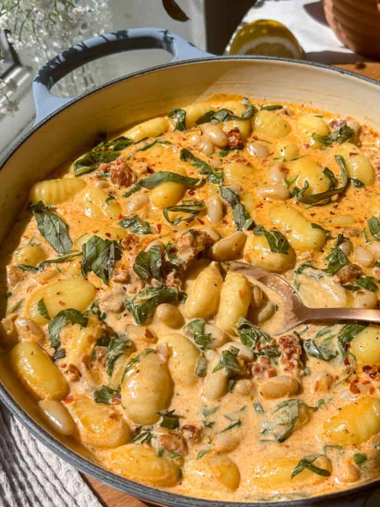 close up shot of pan of marry me gnocchi with white beans, sun-dried tomatoes, basil, creamy sauce