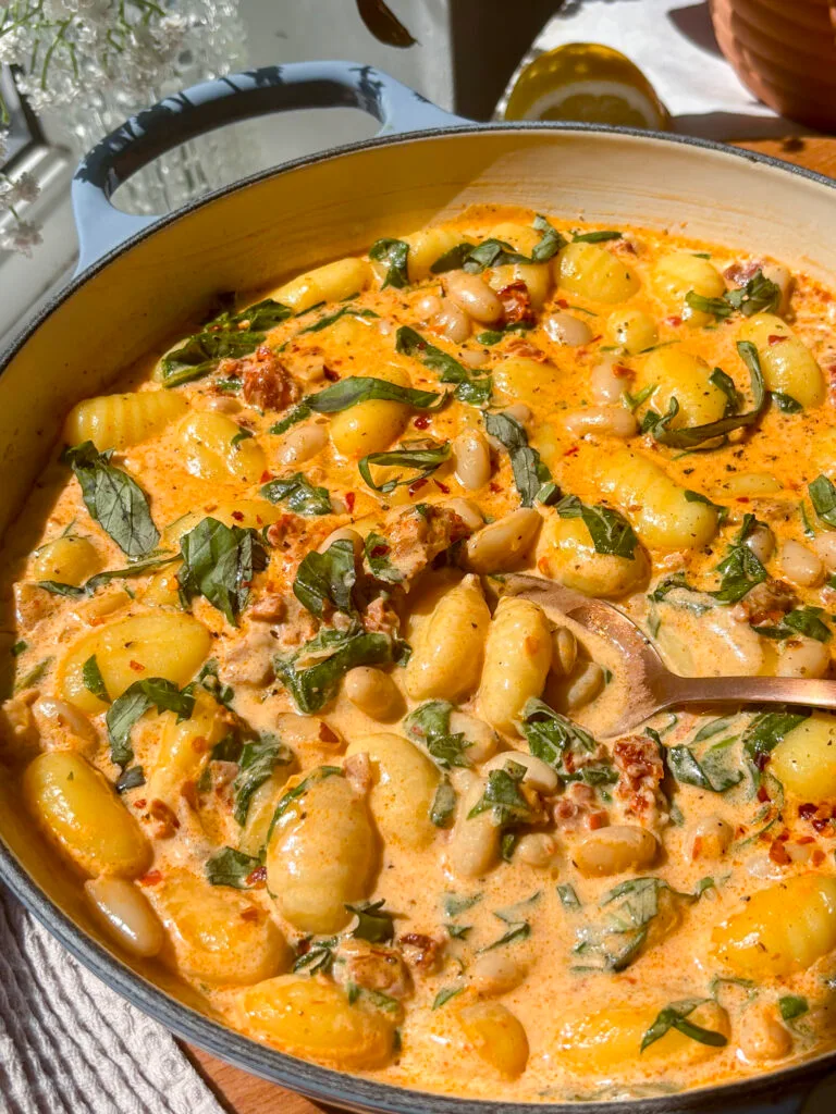 close up shot of pan of marry me gnocchi with white beans, sun-dried tomatoes, basil, creamy sauce