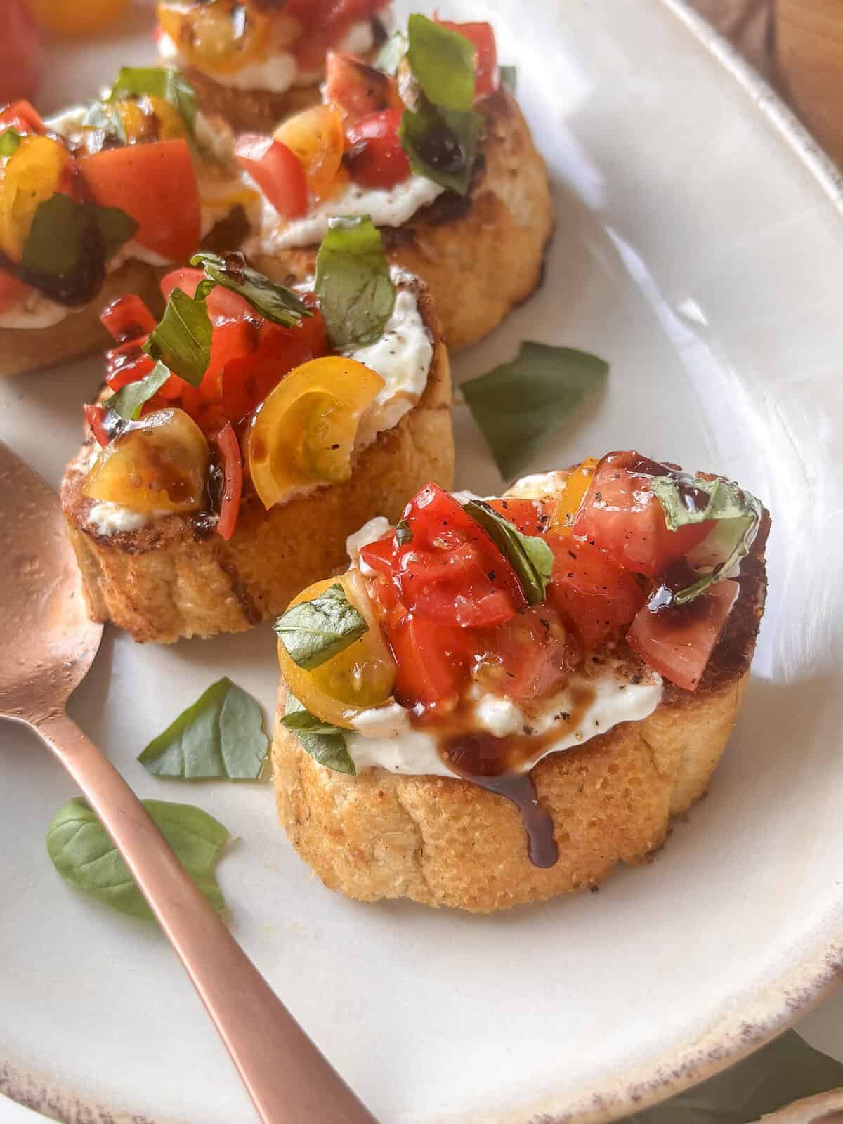 bruschetta on a serving plate, with diced tomatoes, fresh basil, and balsamic glaze