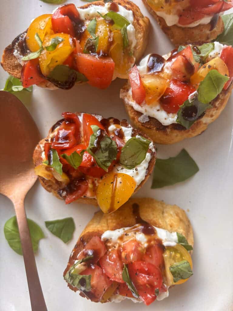 bruschetta on a serving plate, with diced tomatoes, fresh basil, and balsamic glaze