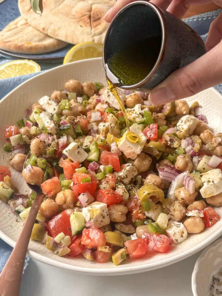 Greek salad in a white bowl, being dressed with olive oil
