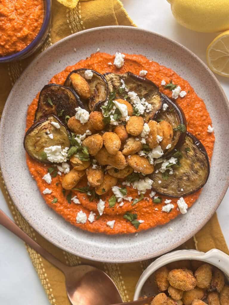 crispy butter beans piled up on top of roasted eggplant and romesco sauce