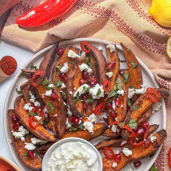 sweet potato wedges loaded with feta, parsley, chilli, and pomegranate with a dip on the side