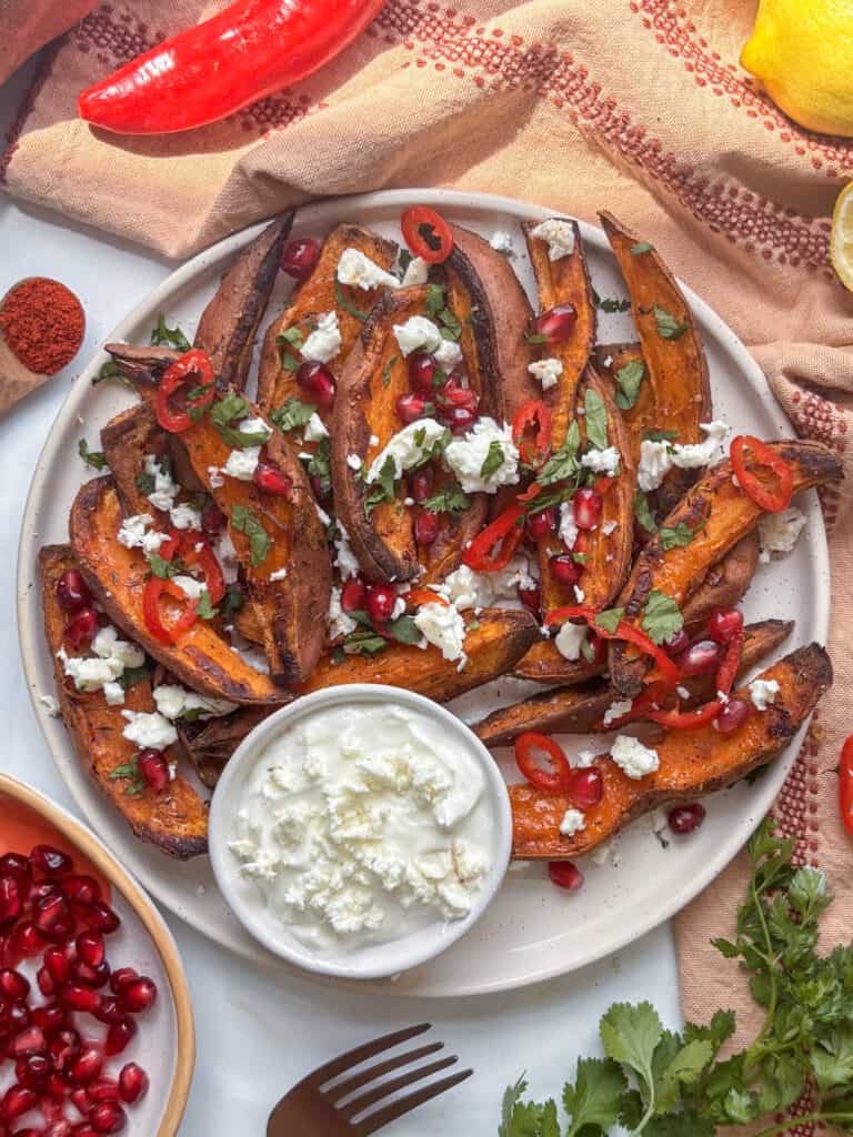 sweet potato wedges loaded with feta, parsley, chilli, and pomegranate with a dip on the side