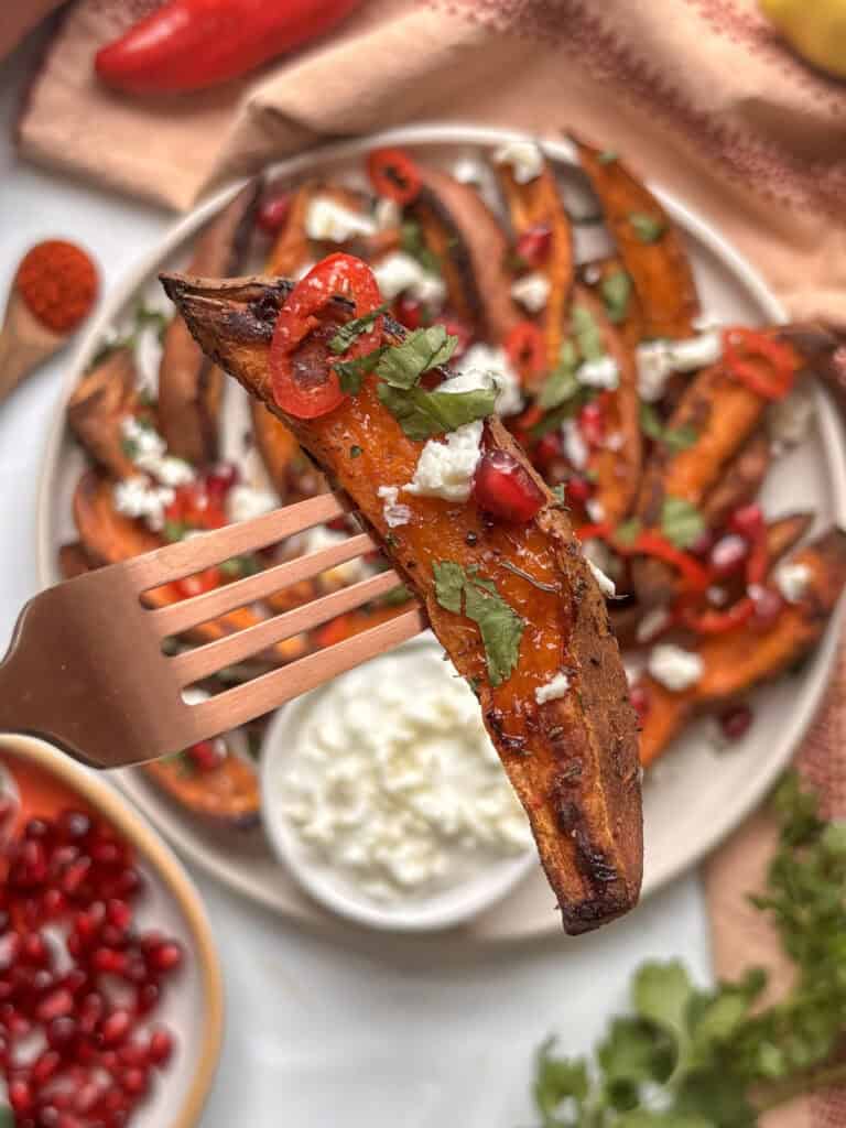 a crispy sweet potato wedge with chilli, parsley, and feta on it held by a fork above the rest of the plate