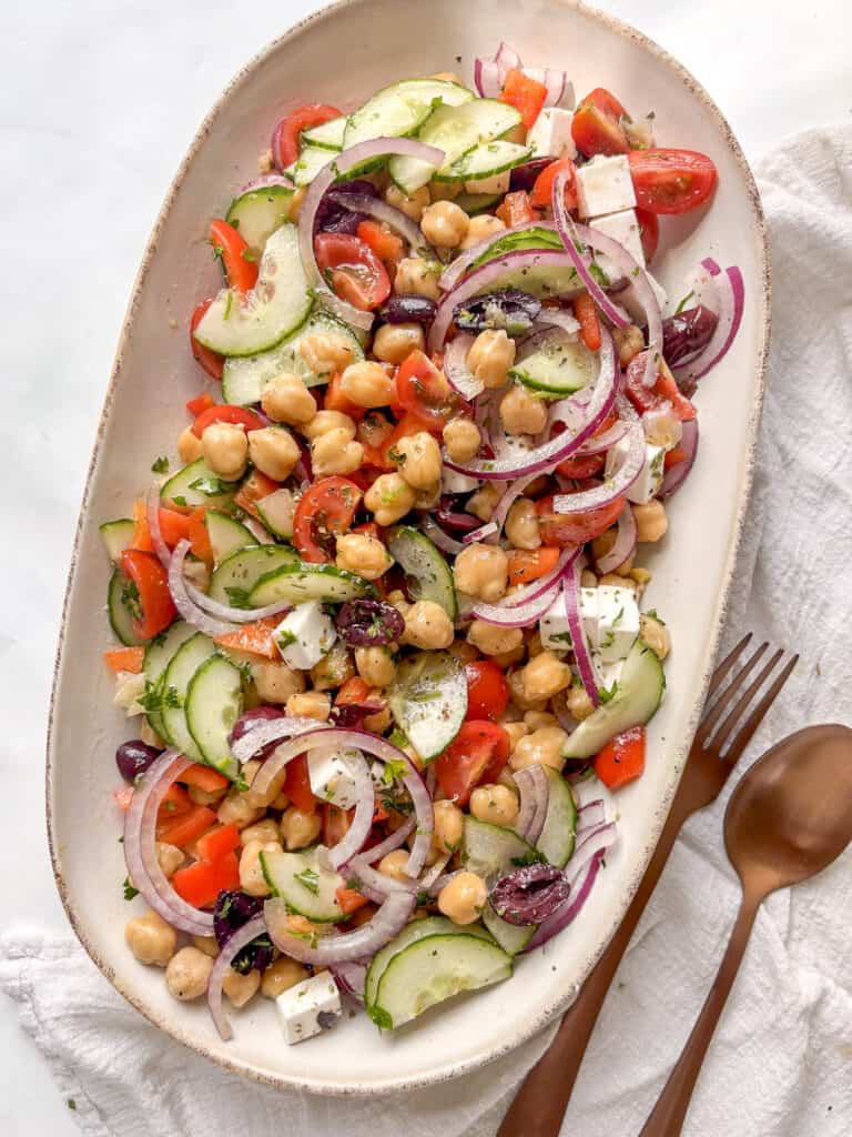 a serving plate of mediterranean chickpea salad with chickpeas, red pepper, tomatoes, red onion, olives, cucumber, and more