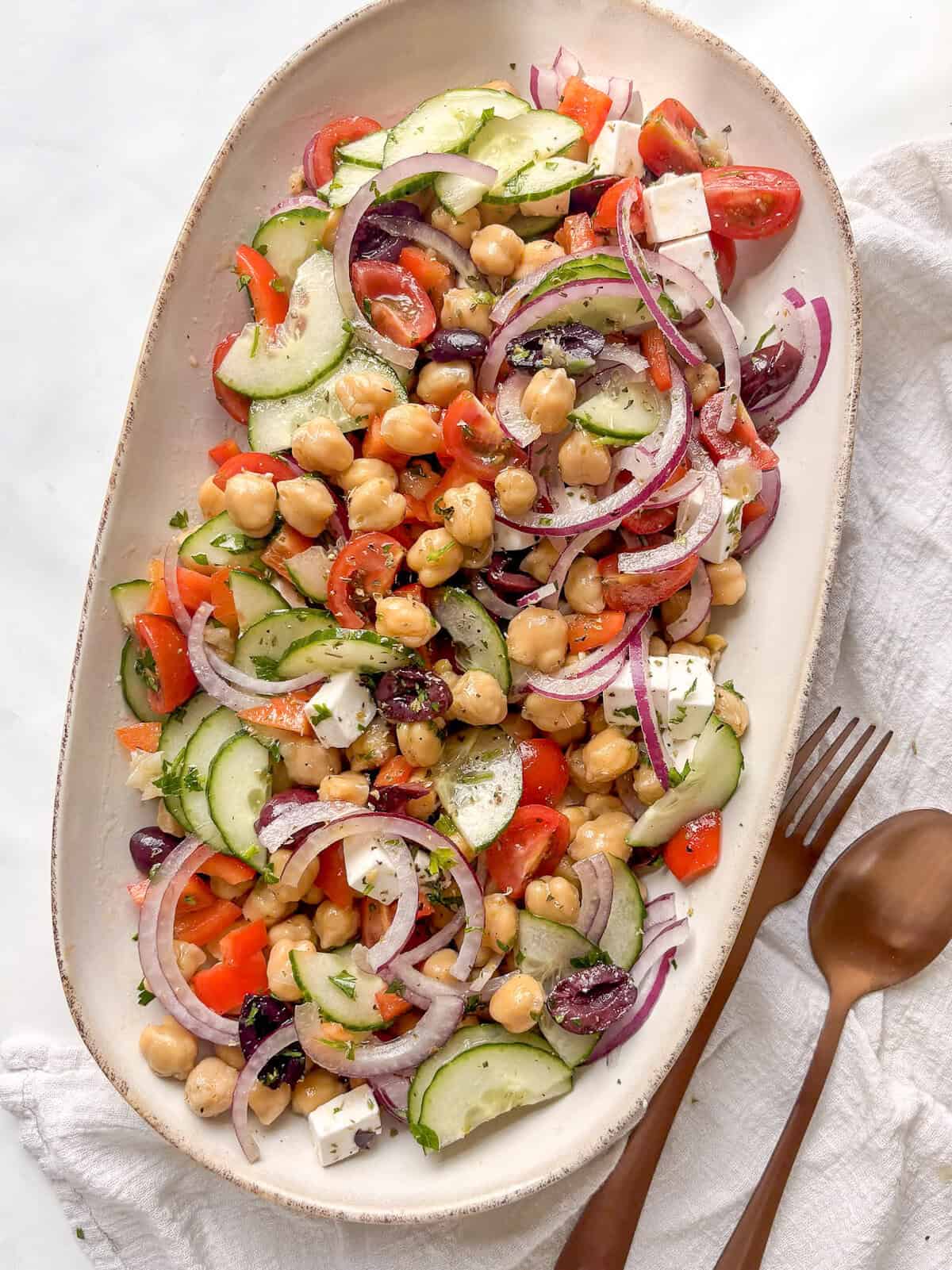 a serving plate of mediterranean chickpea salad with chickpeas, red pepper, tomatoes, red onion, olives, cucumber, and more