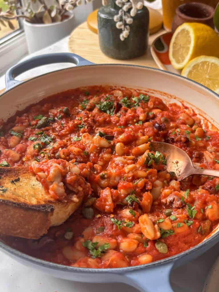 a pan of white bean puttanesca with parsley, olives, and capers