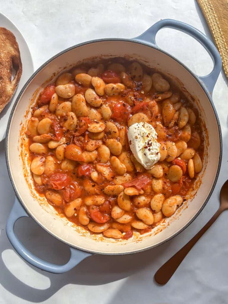 a one-pot casserole dish of rosemary and tomato butter beans with soft cheese and red pepper flakes