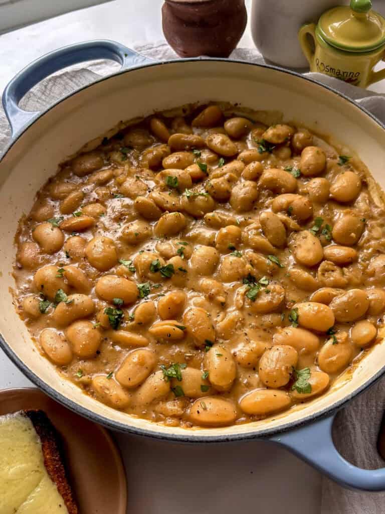 casserole dish of french onion butter beans topped with chopped parsley, on top of a white table cloth