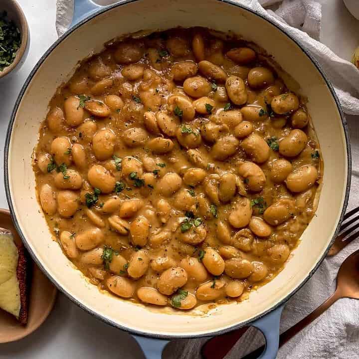 casserole dish of french onion butter beans topped with chopped parsley, on top of a white table cloth and with a slice of cheese on toast on the side