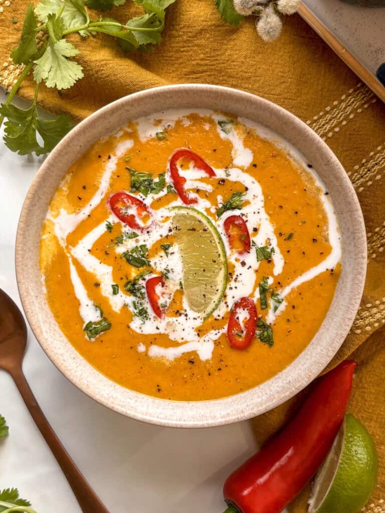 a soup bowl with coconut curry lentil soup made with red curry paste. Coconut cream is drizzled over the top, with red chillies, cilantro, and a lime wedge