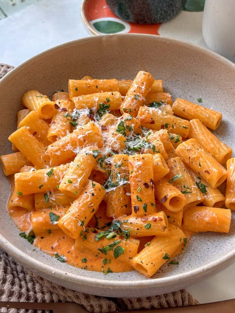 creamy tomato pasta in a grey bowl, topped with herbs and cheese