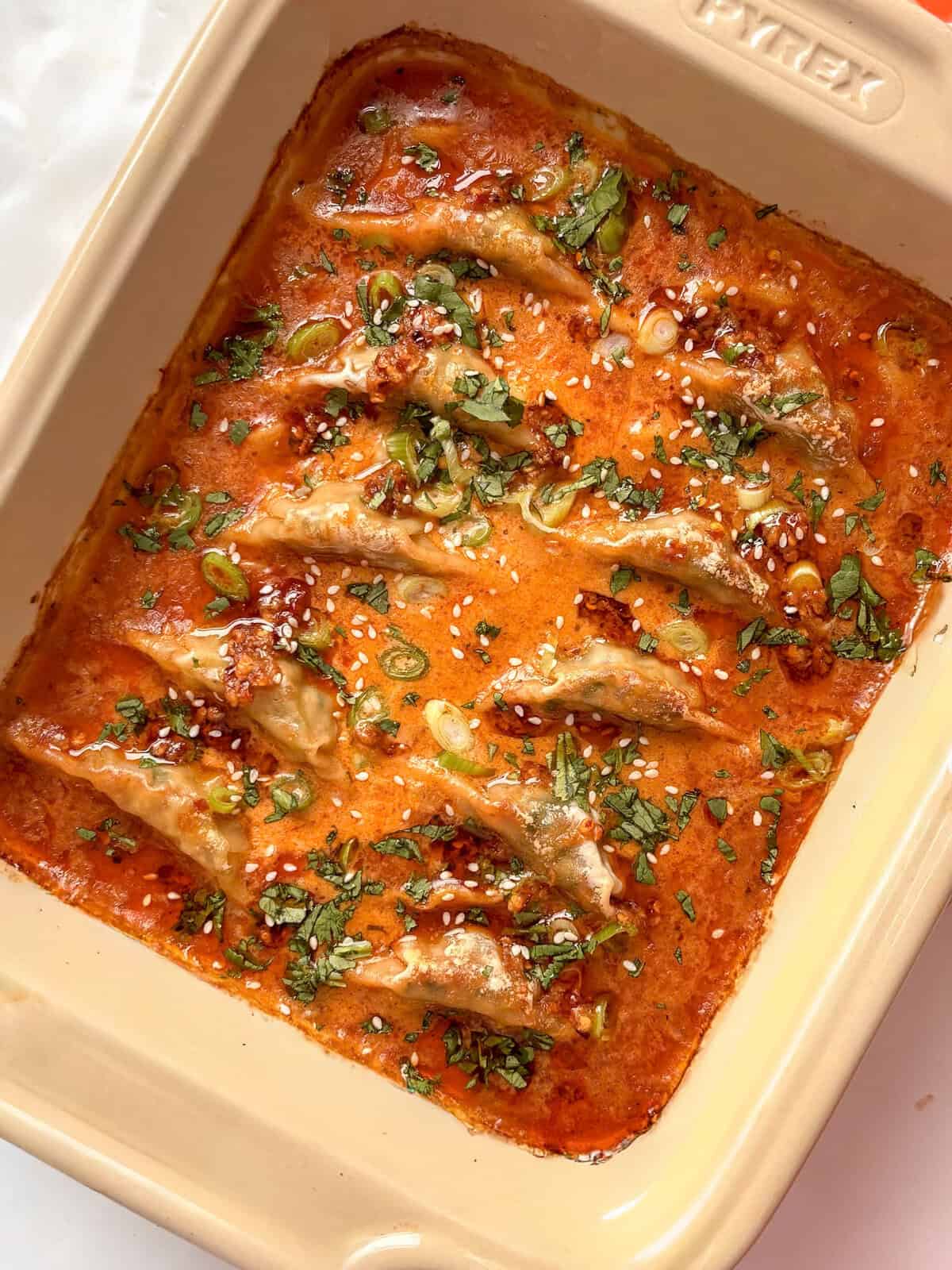 dumplings in a coconut red curry sauce topped with herbs, chili crisp, and sesame seeds