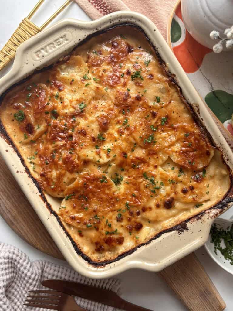 Cheesy marmite potato bake in a casserole dish, topped with green herbs