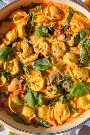 a casserole pan of Marry Me tortellini topped with red chili flakes and fresh basil