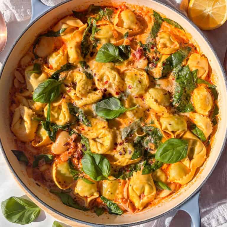a casserole pan of Marry Me tortellini topped with red chili flakes and fresh basil