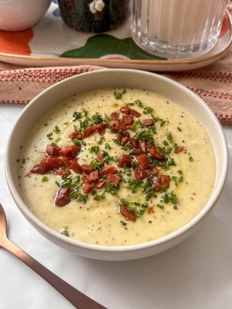 a creamy bowl of potato and leek soup drizzle with olive oil and black pepper, and topped with a garnish of crispy vegan bacon and chopped chives.