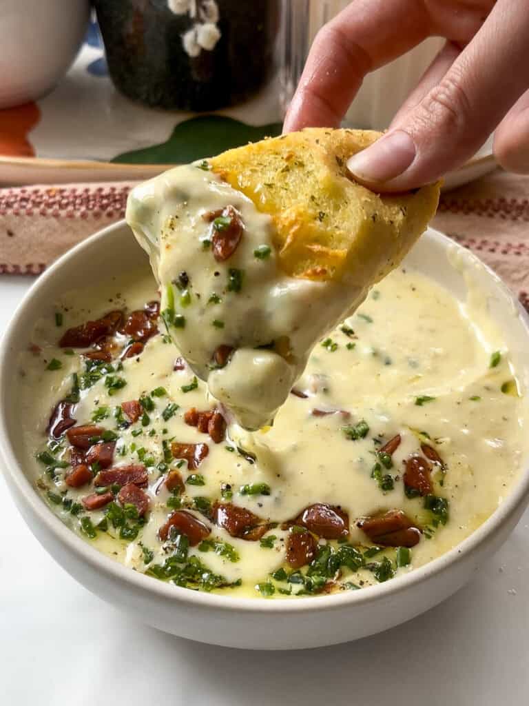 a slice of bread having been dipped in the potato and leek soup (which can be seen in the background), coating in the soup and the garnish of chives