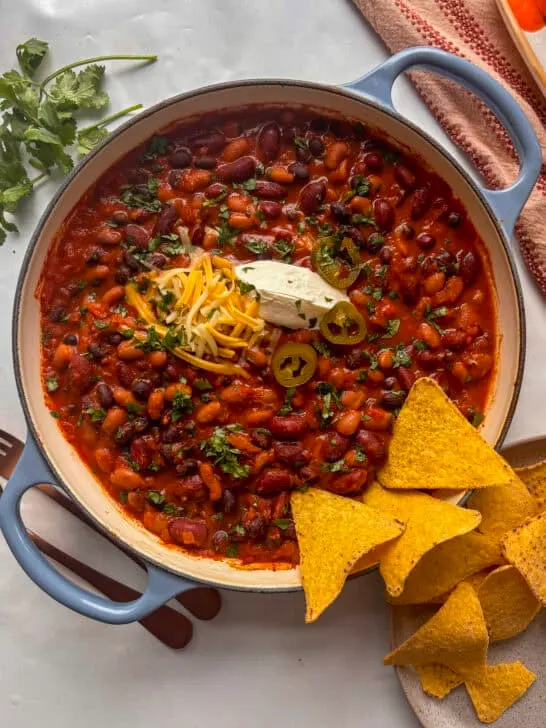 Smoky three bean chili recipe topped with sourcream and cheese, and tortilla chips