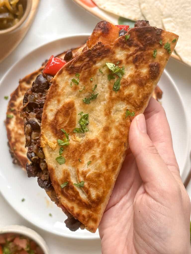 a crispy black bean and sweet potato taco held up to the camera - topped with chopped cilantro and with the filling of blakc beans, red pepper, and sweet potato peeking out