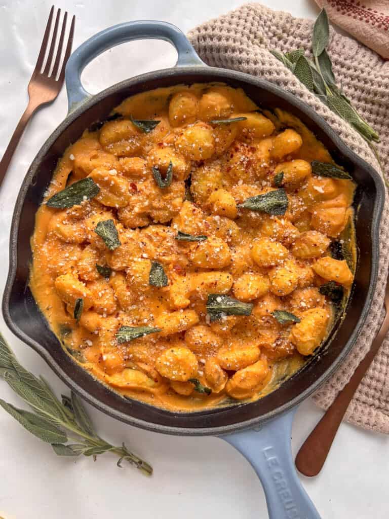 a skillet of butternut squash gnocchi topped with fried sage and grated Pecorino cheese