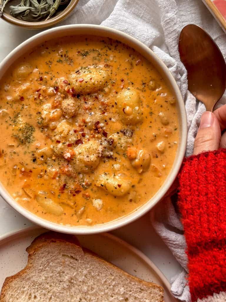 a delicious creamy gnocchi soup in a white bowl topped with red pepper flakes, cheese, and herbs