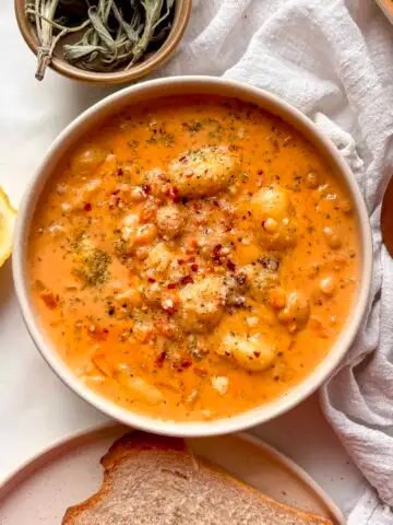 creamy gnocchi soup in a white bowl, topped with cheese and red pepper flakes