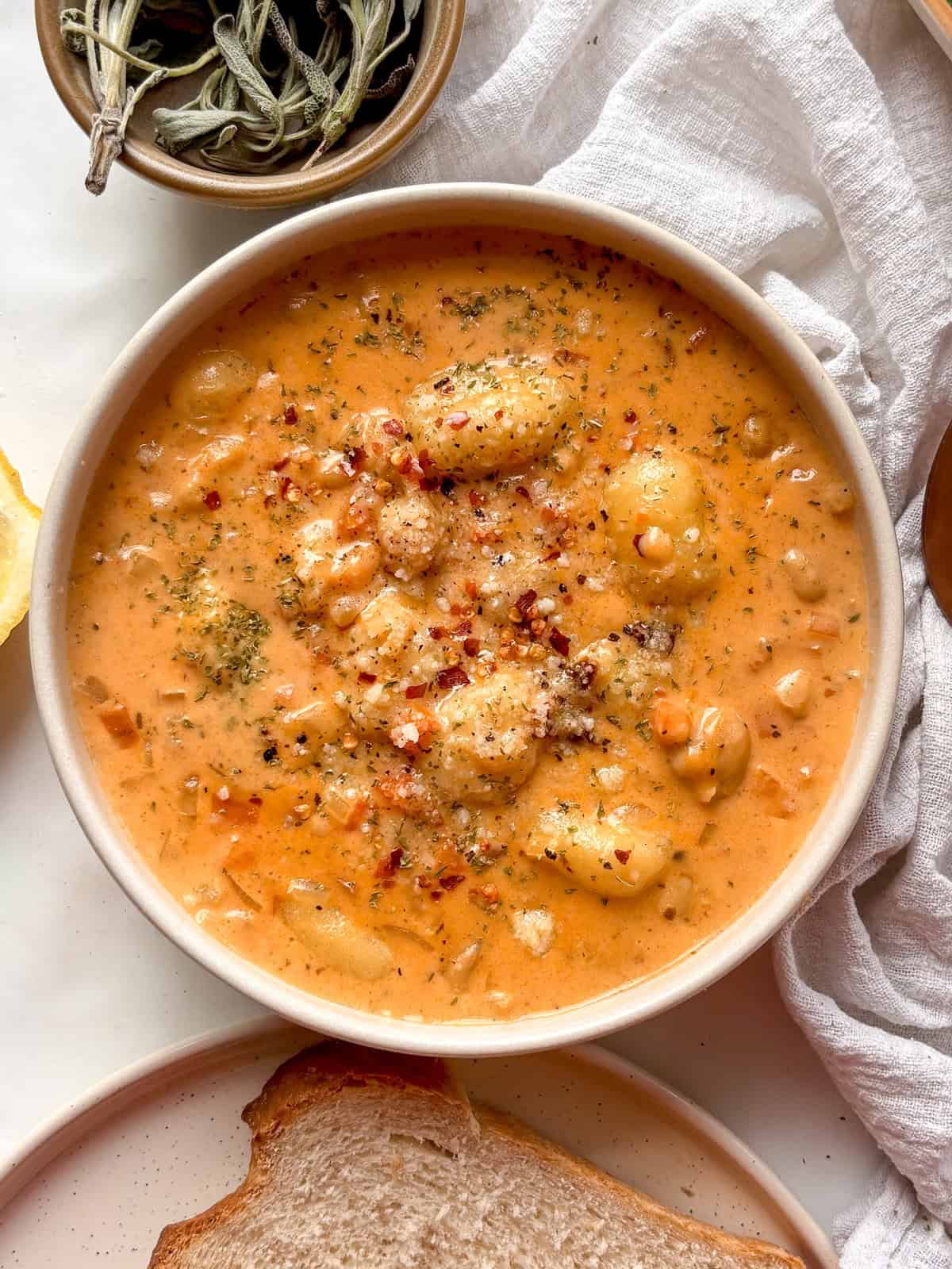 creamy gnocchi soup in a white bowl, topped with cheese and red pepper flakes