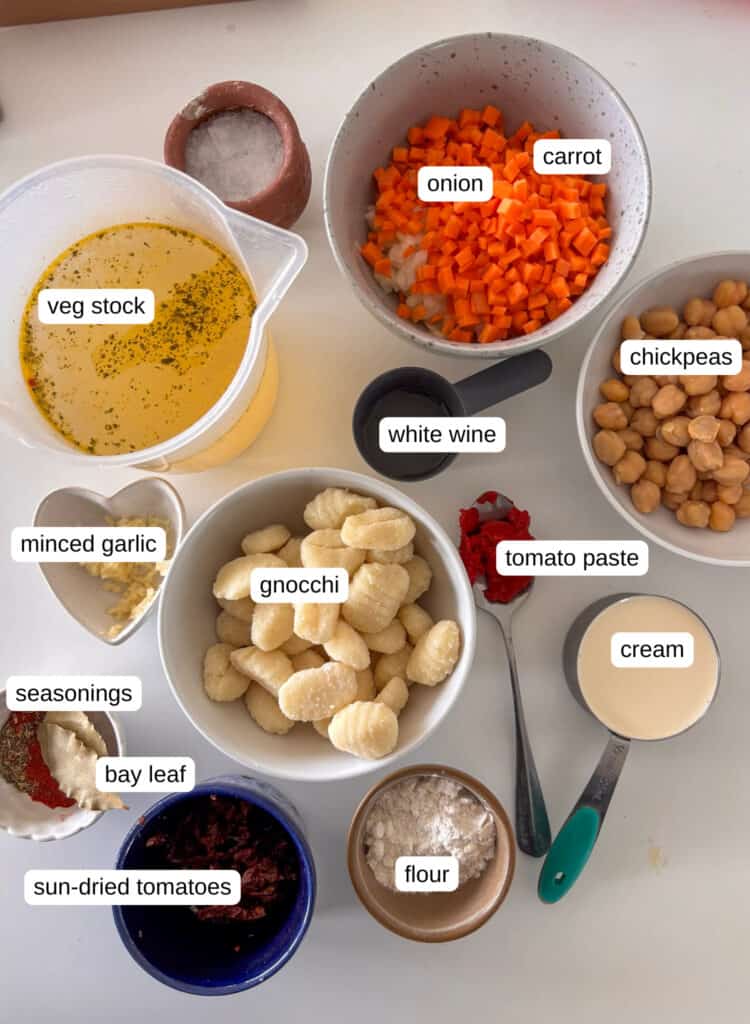 ingredients shot for this gnocchi soup - bowls laid out with each individual ingredient. Includes onion and carrot, chickpeas, white wine, veg stock, minced garlic, gnocchi, tomato paste, cream, seasonings, bay leaves, sun-dried tomatoes, and flour