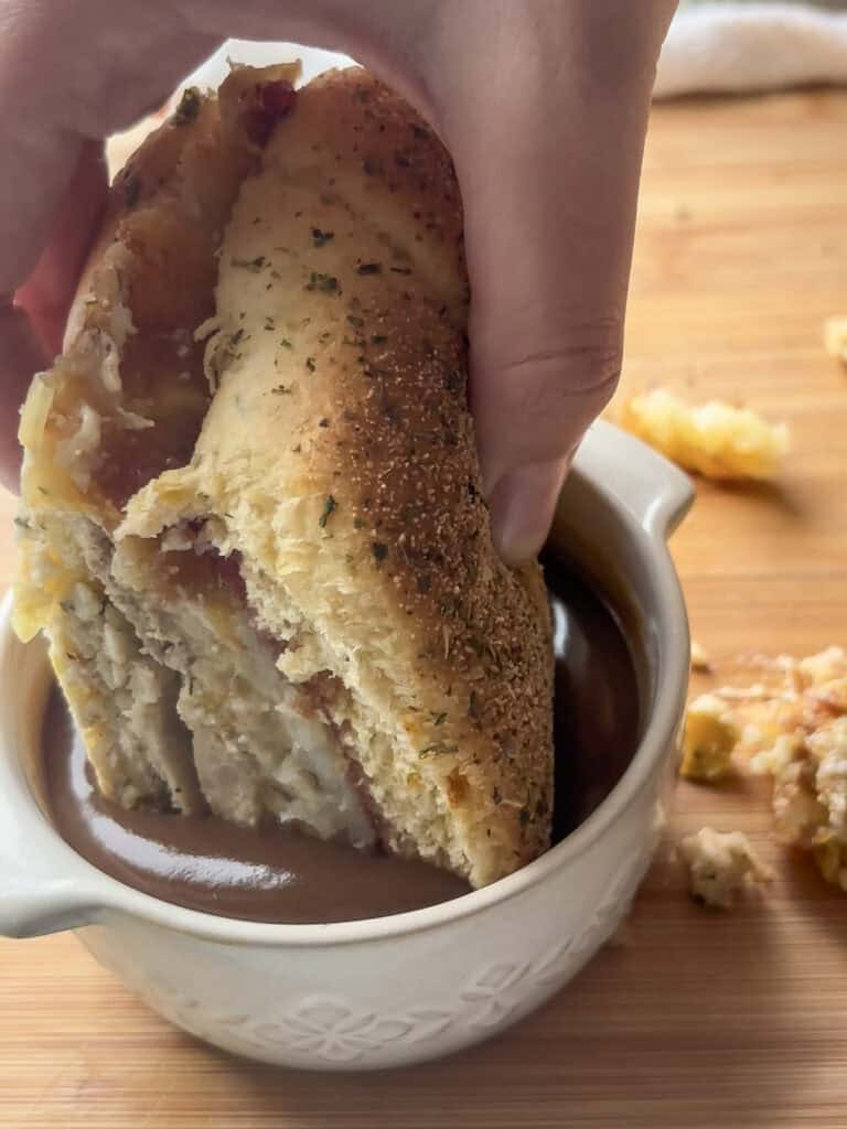 festive christmas sandwich being dipped in a pot of gravy