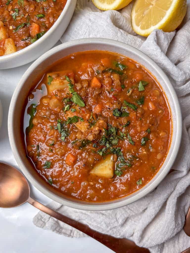 a bowl of lentil soup with potatoes and carrots, shopped with fresh parsley