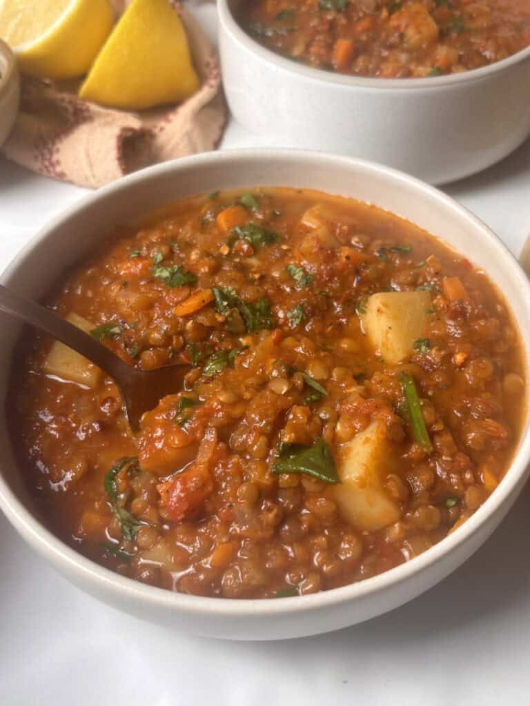 bowl of lentil soup with a spoon, topped with fresh chopped parsley