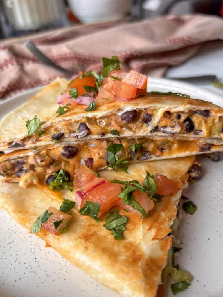 a stack of cheesy black bean quesadillas, topped with diced tomatoes, red onion, and diced cilantro