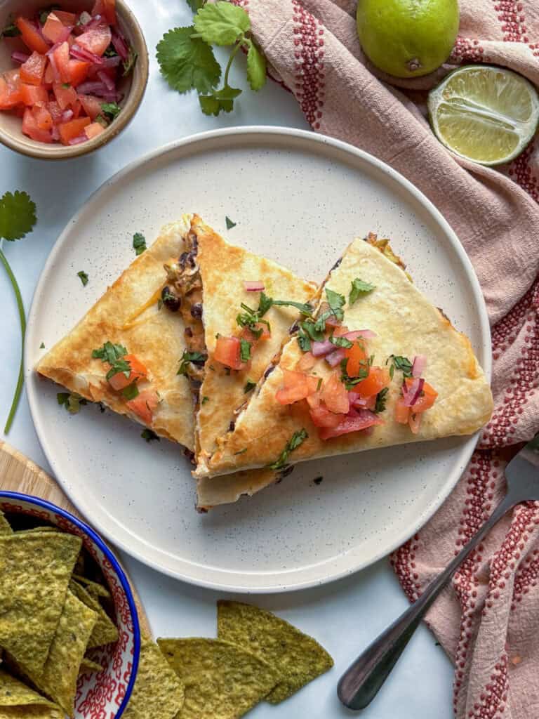 a plate of crispy black bean quesadillas topped with diced tomatoes, red onion, and cilantro