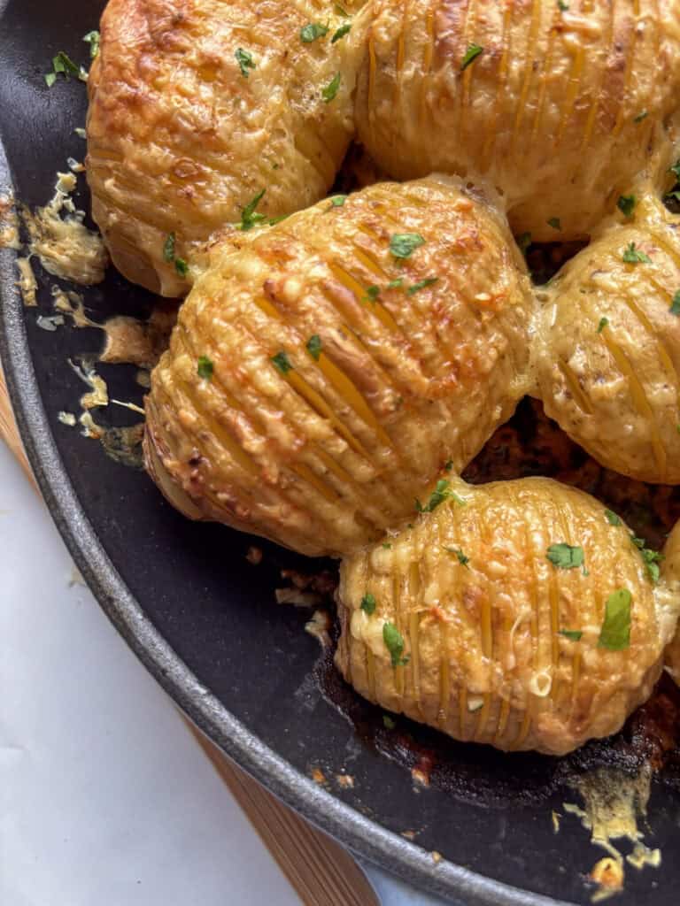 cheesy garlic hasselback potatoes in a skillet topped wuth parsley