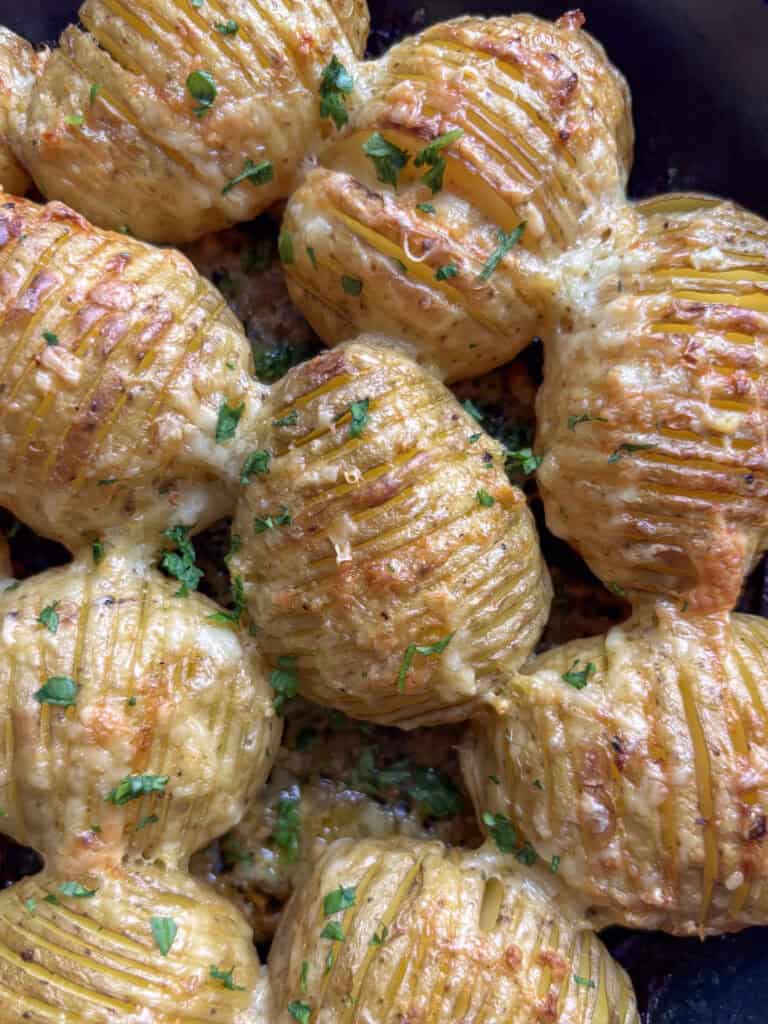 cheesy garlic hasselback potatoes in a skillet topped wuth parsley